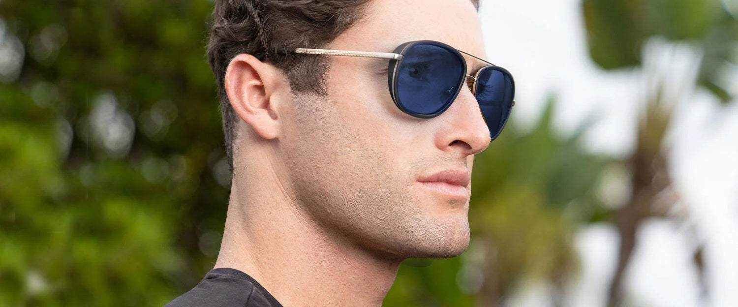 A man in Gunnar Dume Sunglasses, featuring GUNNAR technology for blue light protection, looks to the side against a blurred green and sky backdrop.