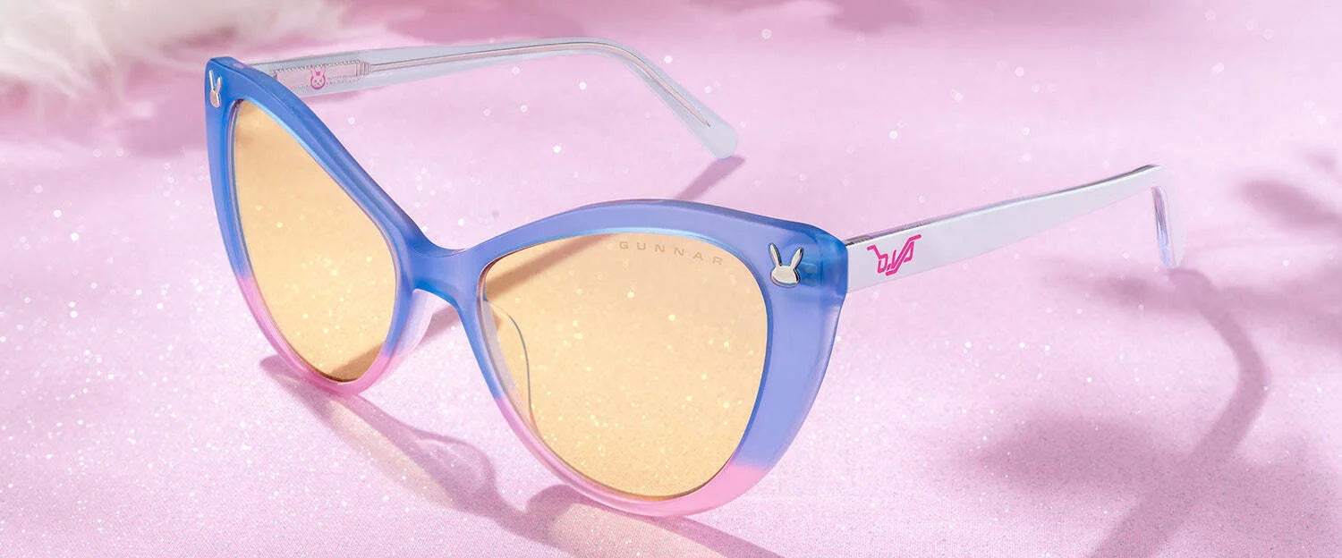 Gunnar Overwatch D.Va Tokki Edition Computer Glasses feature a cat-eye design with pink and blue frames, tinted lenses, and a sparkly pink finish.