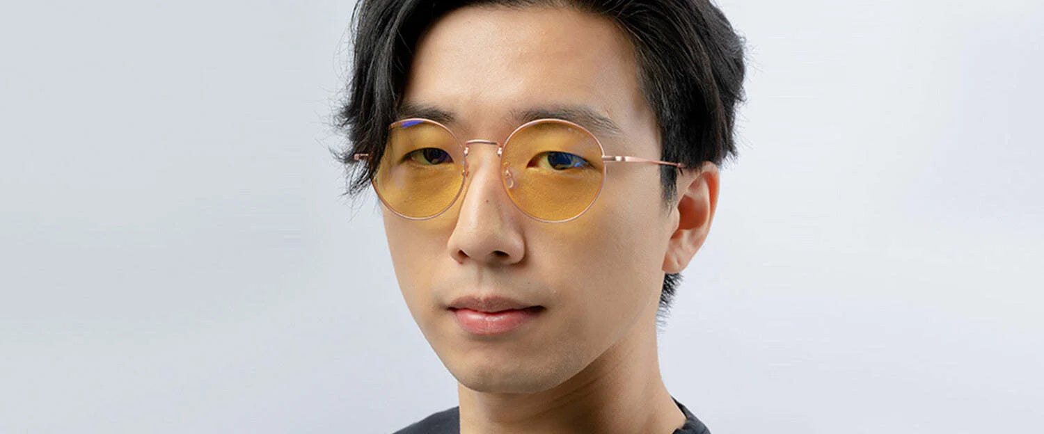 A person wearing Gunnar Ellipse Computer Glasses, featuring round yellow-tinted lenses and a sleek stainless-steel frame, paired with a black shirt against a light gray background.