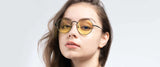 Wearing Gunnar Ellipse Computer Glasses with a stainless steel frame and round yellow-tinted lenses, a woman confidently looks at the camera against a neutral background.