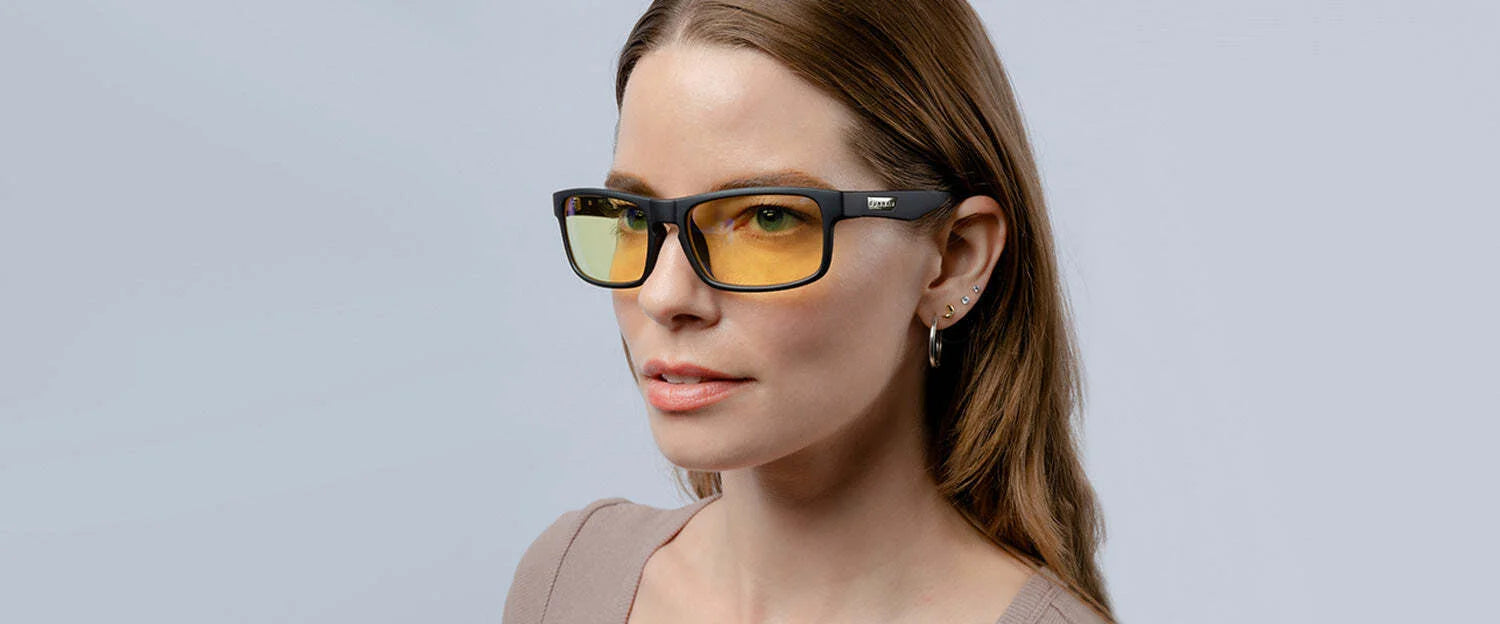 A woman wearing Gunnar Enigma Computer Glasses, size 58, and earrings stands against a gray background.