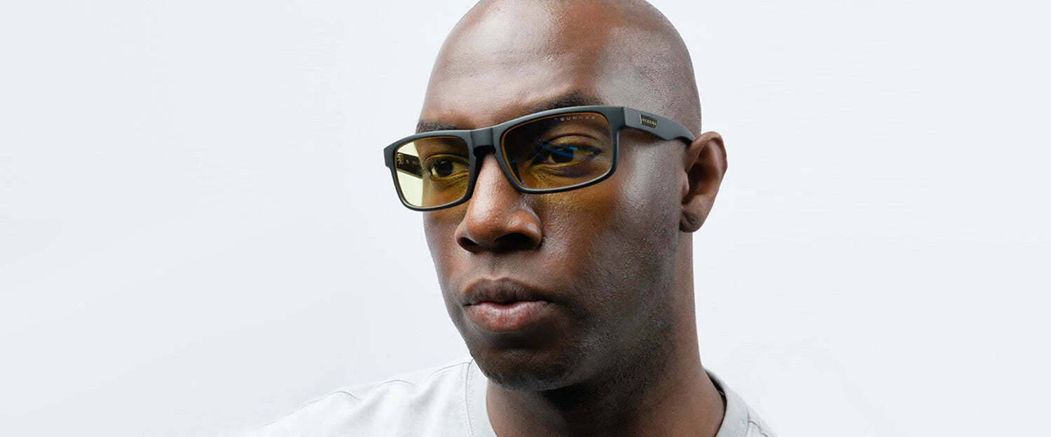 A man wearing Gunnar Enigma Computer Glasses, featuring a black frame and yellow lenses, gazes to the side against a plain background.