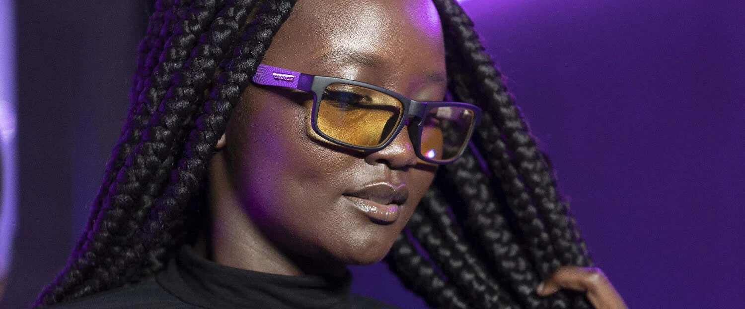 Against a purple-lit backdrop, a braided individual wears Gunnar's Enigma Black Panther Edition Computer Glasses, size 58, with patented lens technology for exceptional blue light protection.