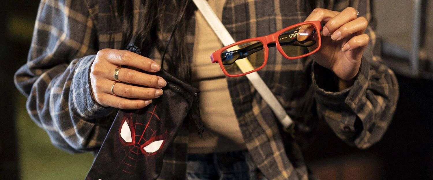 A person in a plaid shirt holds Gunnar Enigma Spider-Man Miles Morales Edition computer glasses with a durable nylon frame and a black pouch.