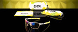 Gunnar ESL Blade Lite Computer Glasses, size 55, blend yellow and green accents with amber lens tech to reduce digital eye strain. Comes with an ESL-branded case and a cleaning cloth, elegantly displayed on a reflective surface.