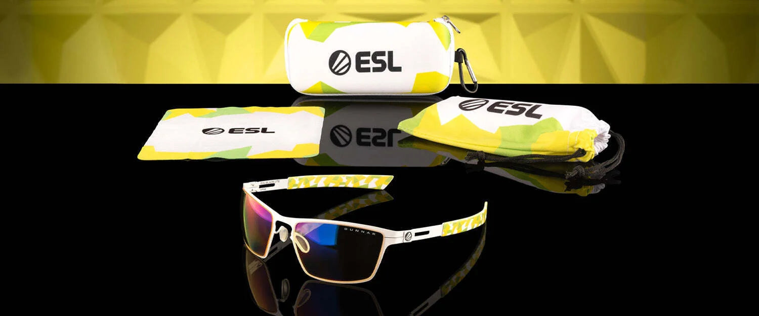 Gunnar ESL Blade Lite Computer Glasses, size 55, blend yellow and green accents with amber lens tech to reduce digital eye strain. Comes with an ESL-branded case and a cleaning cloth, elegantly displayed on a reflective surface.