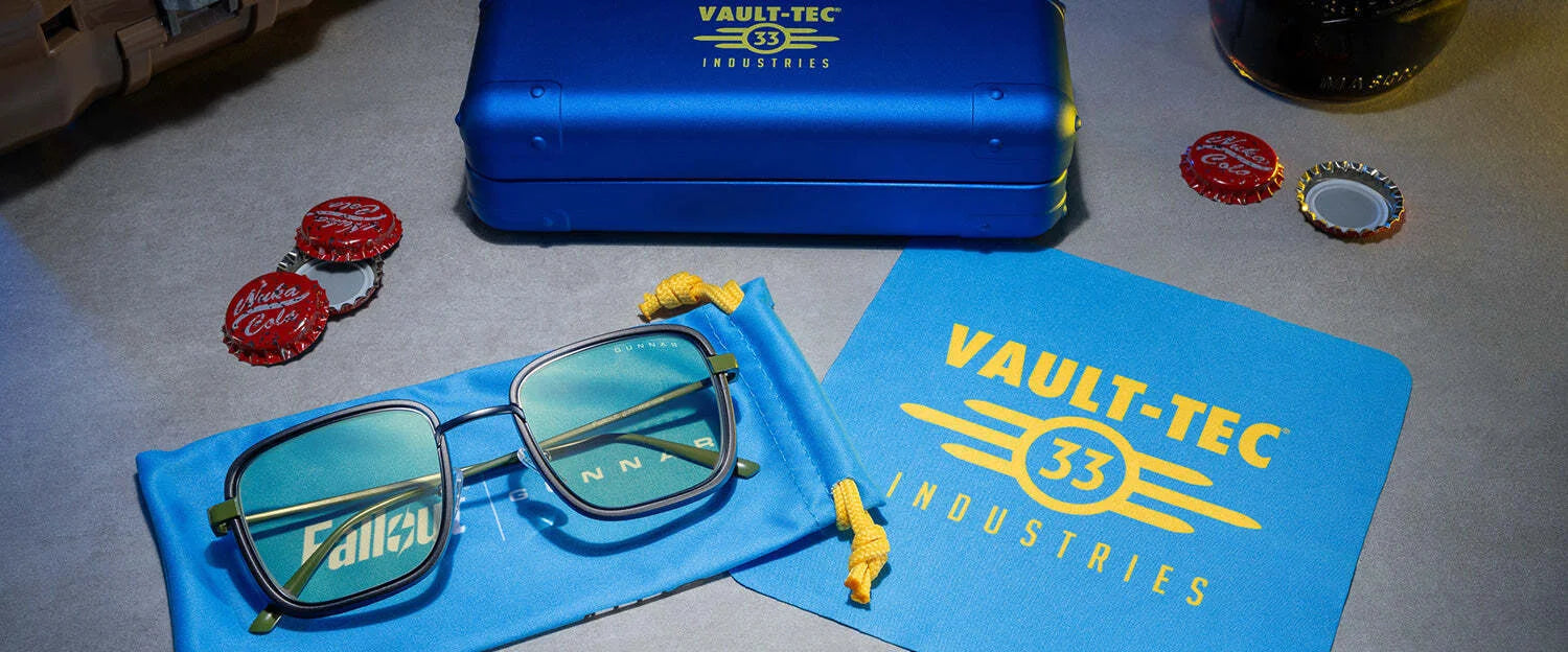 A pair of Gunnar Fallout Vault 33 Computer Glasses (size 52) is displayed with its case and cloth, amid Nuka-Cola bottle caps on the table. These glasses offer a retro-futuristic design while effectively blocking blue light.