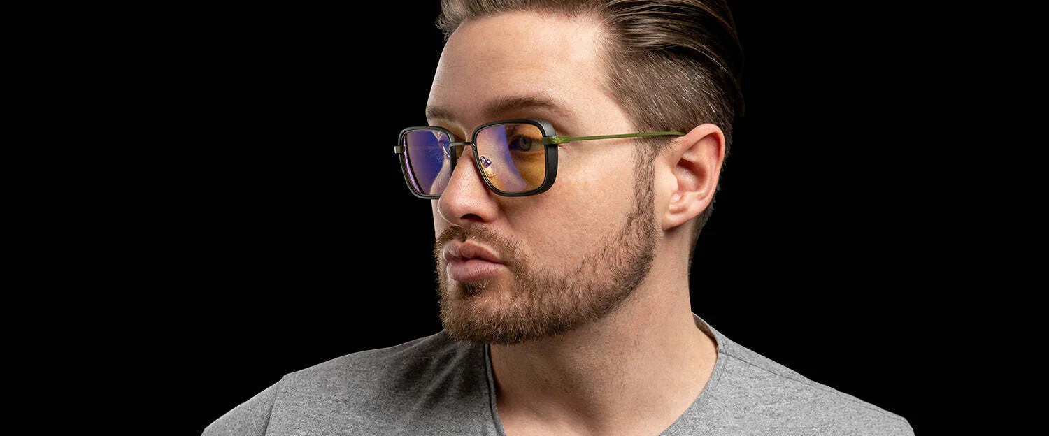 Bearded individual looking left against a black background, wearing a gray shirt and Gunnar Fallout Vault 33 Computer Glasses by Gunnar, featuring retro-futuristic design.