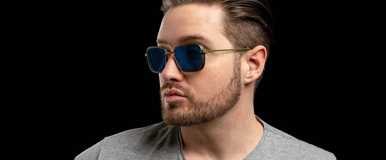 A man exudes cool confidence in Gunnar Fallout Vault 33 Sunglasses, Size 52, and a gray shirt against a black backdrop. The retro-futuristic square frames enhance his style while Gunnar's lens technology provides comfort and clarity.