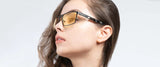 A woman with long hair wears Gunnar Fremont Computer Glasses, made of stainless steel and acetate, featuring yellow-tinted lenses that block blue light, as she gazes to the side against a plain background.