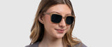 A woman with wavy hair smiles subtly in Gunnars from the Groot Marvel Edition, featuring large square lenses, against a plain background.