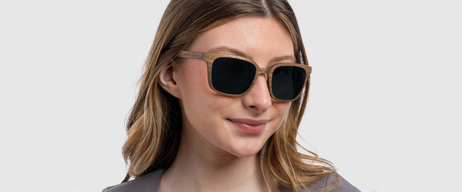 A woman with wavy hair smiles subtly in Gunnars from the Groot Marvel Edition, featuring large square lenses, against a plain background.