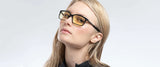 A person with long blonde hair wears Gunnar Haus Computer Glasses featuring yellow-tinted, anti-reflective lenses and a black top against a plain background.