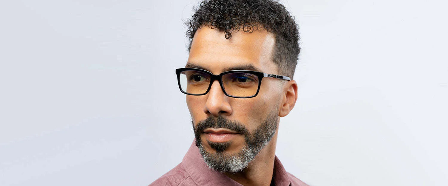 A man with curly hair and glasses gazes sideways against a plain background, wearing a maroon shirt. His Gunnar Haus Reading Computer Glasses, size 53, crafted from European materials, add sophistication while providing blue light blocking for modern comfort.