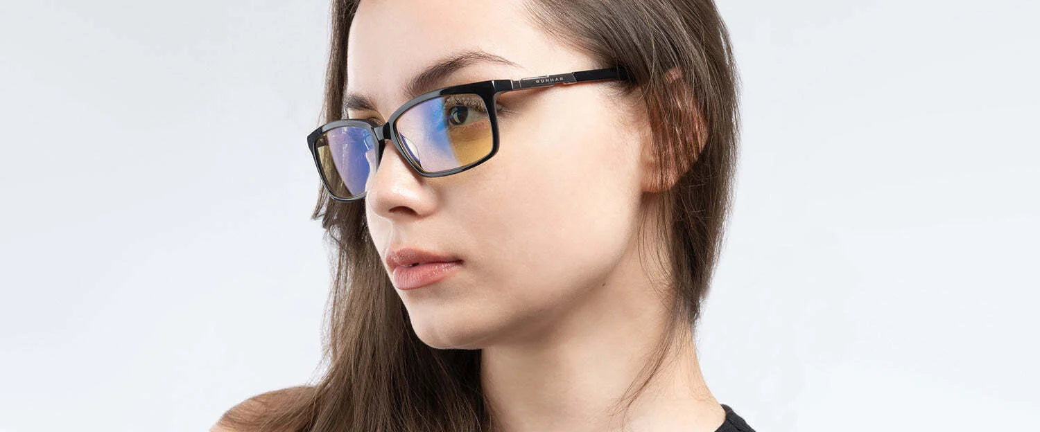 A person with long hair, donning Gunnar Haus Computer Glasses by Gunnar, featuring anti-reflective lens coatings, gazes thoughtfully to the side against a light gray background.