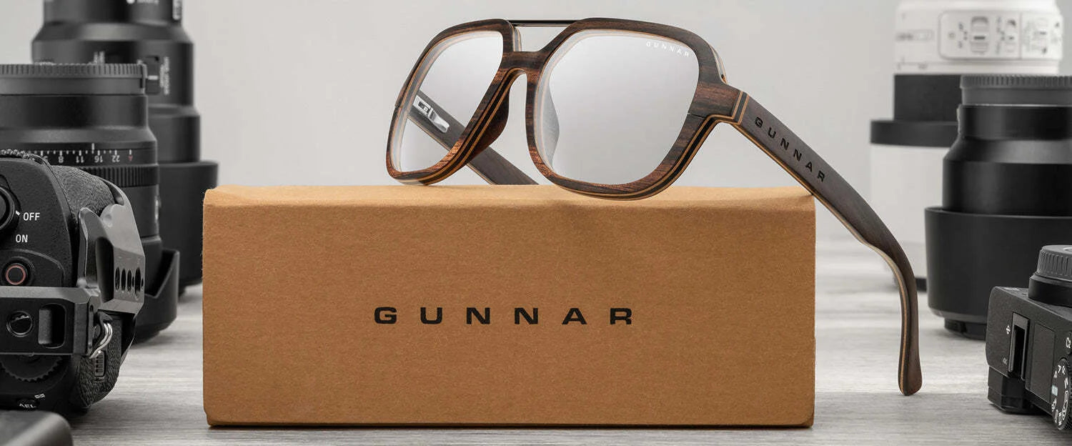Gunnar Humboldt Computer Glasses, featuring GUNNAR lens technology, rest on a box surrounded by camera lenses on a wooden surface.