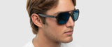 A person casts a sideways glance wearing Gunnar Humboldt Sunglasses | Size 54, showcasing sleek aviator-style blue lenses, paired with a plain white shirt.