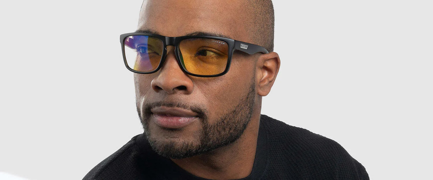 A man, dressed in a black sweater, gazes to the side against a light gray background wearing yellow-tinted Gunnar Intercept Reading Computer Glasses size 58 with durable nylon frames and blue light protection.