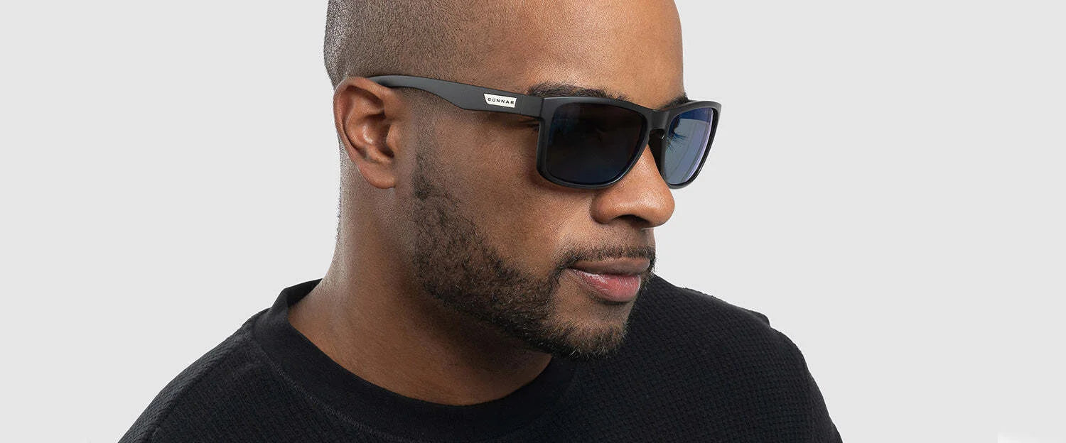 A man stands confidently against a plain background, sporting Gunnar Intercept Sunglasses with anti-reflective lenses and a black sweater.