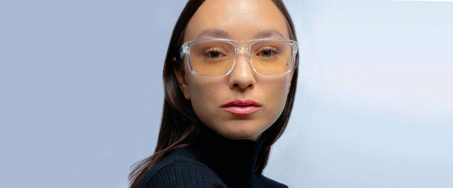 A person wearing Gunnar Intercept Computer Glasses with blue light protection stands confidently with clear glasses, dark hair, and a black turtleneck against a light blue background.