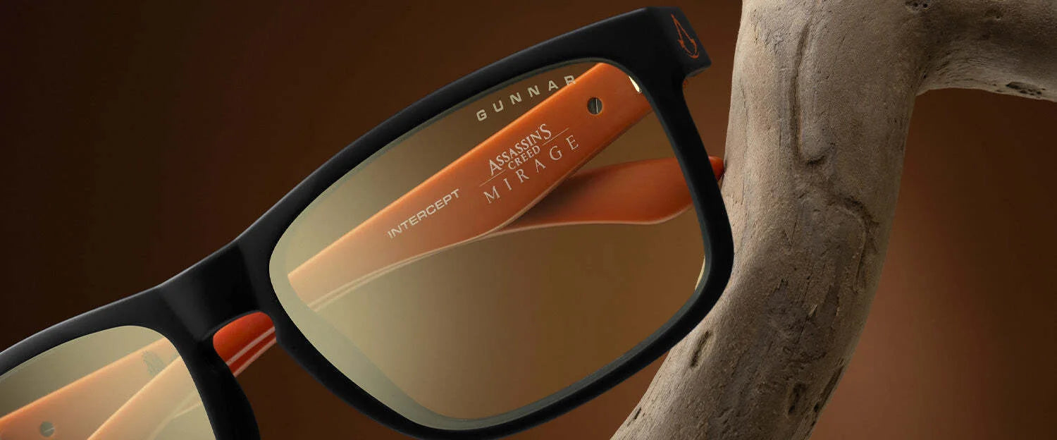 A close-up of sleek black and orange Gunnar Intercept Assassin’s Creed Mirage Edition Computer Glasses, featuring "Gunnar" and "Assassin's Mirage" text on the lenses with blue light protection.