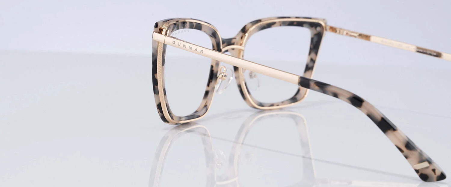 The Gunnar Kaia Computer Glasses | Size 53 offer a modern square tortoiseshell frame with slim beige temples, reflecting on a shiny white surface.