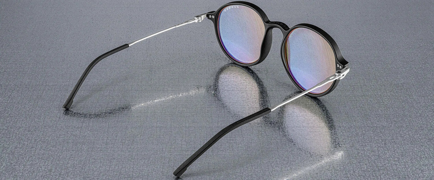 Gunnar Loop Computer Glasses, featuring black frames and thin silver arms, reflect light on a textured gray surface. Enhanced with GUNNAR lens technology for optimal productivity.