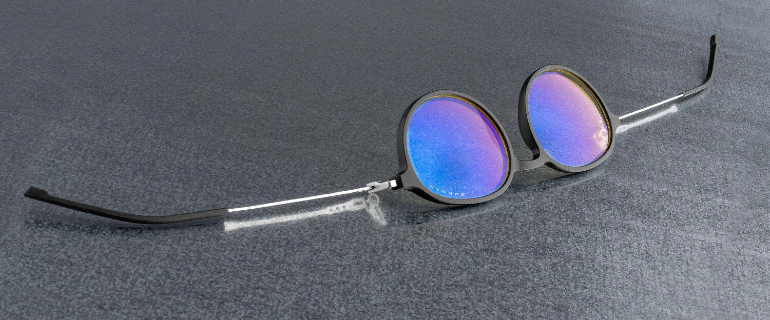 Gunnar Loop Computer Glasses, Size 51, featuring metallic frames and purple-tinted lenses, rest on a gray surface. Equipped with Gunnar lens technology to filter blue light, they enhance both style and productivity.