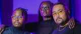 Three individuals wearing Gunnar Mateo Black Panther Vibranium Edition Computer Glasses with patented lens technology stand in a neon-lit room, their serious expressions intensified by the sleek, lightweight frames.