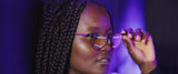 A person with braided hair adjusts their Gunnar Mateo Black Panther Vibranium Edition Computer Glasses, characterized by a lightweight titanium frame and a soft purple glow.