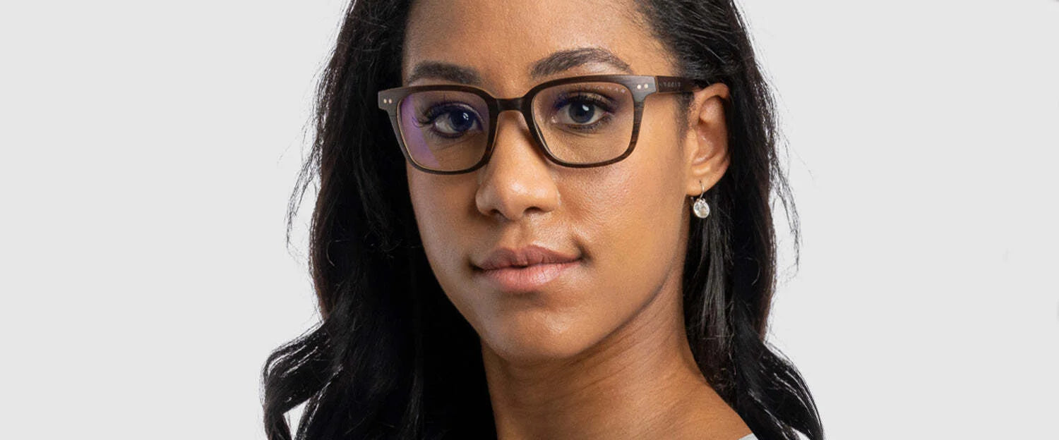 A person with long black hair wears Gunnar Muir Computer Glasses in Size 50, crafted from sustainably harvested ebony wood, and looks into the camera against a plain background.