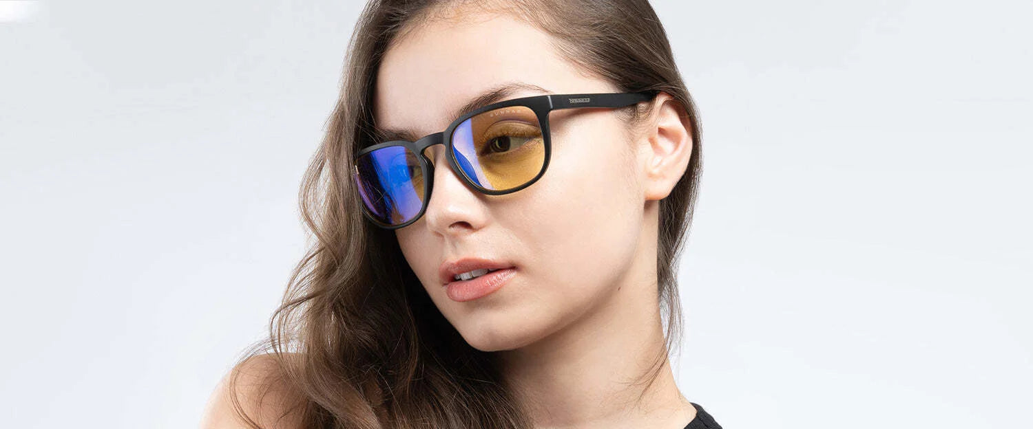 A person wearing Gunnar Oakland Computer Glasses with a durable nylon frame and tinted lenses, their long hair flowing as they glance sideways. The glasses offer stylish flair and blue light protection, all set against a plain background.