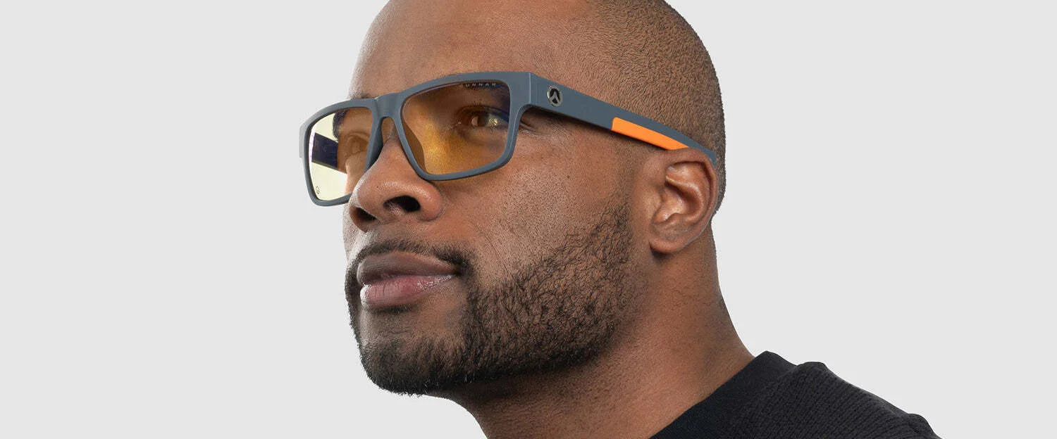 A person wearing Gunnar Overwatch Ultimate Computer Glasses with orange accents and styled with GUNNAR technology, paired with a black shirt, is looking to the side.