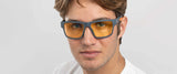 Wearing Gunnar Overwatch Ultimate Computer Glasses with orange-tinted lenses and a white shirt, a person stands against a neutral background.