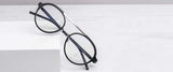 Gunnar Pacifica Computer Glasses in size 50, featuring black round thin frames and blue light blocking technology, sit elegantly on a white surface, showcasing their minimalist design.