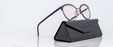 Gunnar Palomar Computer Glasses, featuring round black and pink frames, elegantly rest on a sleek closed black case. Positioned artistically on a pristine white marble surface, they showcase style with the added benefit of blue light blocking technology.
