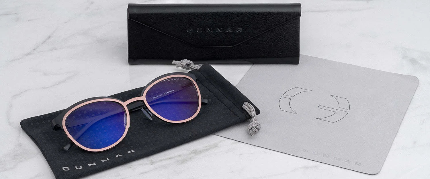 Gunnar's Palomar Computer Glasses with blue lenses, echoing a round glasses style, are placed on a pouch next to a cleaning cloth and case on a marble surface.