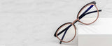 Gunnar Palomar Computer Glasses, Size 51, with round pink rims and black temples, rest elegantly on a white marble surface, showcasing Gunnar's expertise in blue light blocking technology.