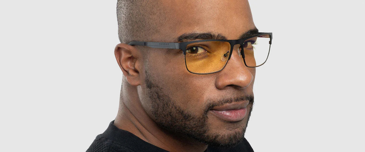 A man in Gunnar Pendleton Computer Glasses, size 57, with yellow-tinted lenses and a black shirt confidently gazes at the camera against a gray backdrop.