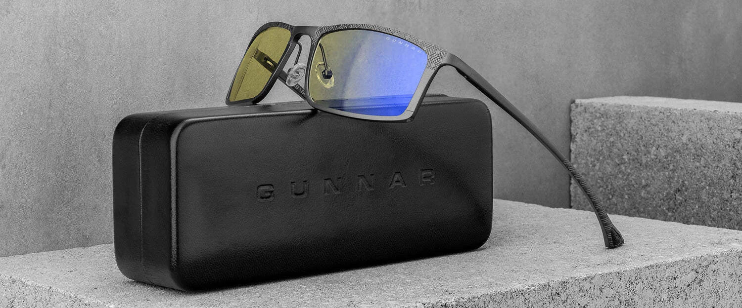 Gunnar Plaid Computer Glasses with reflective lenses, crafted from a lightweight magnesium-aluminum alloy, rest elegantly on a concrete surface inside their black case.