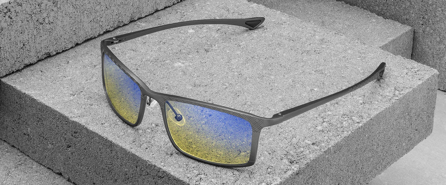 Gunnar Plaid Computer Glasses by Gunnar, featuring rectangular reflective blue-yellow lenses, rest on a textured gray stone surface, crafted from lightweight magnesium-aluminum alloy for both durability and style.