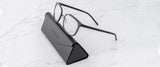 A pair of Gunnar Pismo Computer Glasses | Size 50, with black rims, elegantly rests on a triangular black case on a white marble surface, designed to protect your eyes from harmful blue light.