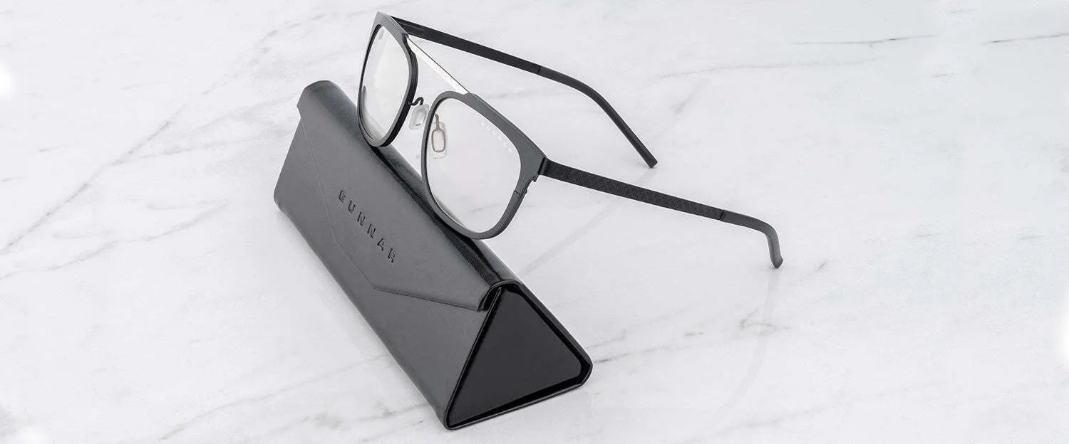 A pair of Gunnar Pismo Computer Glasses | Size 50, with black rims, elegantly rests on a triangular black case on a white marble surface, designed to protect your eyes from harmful blue light.