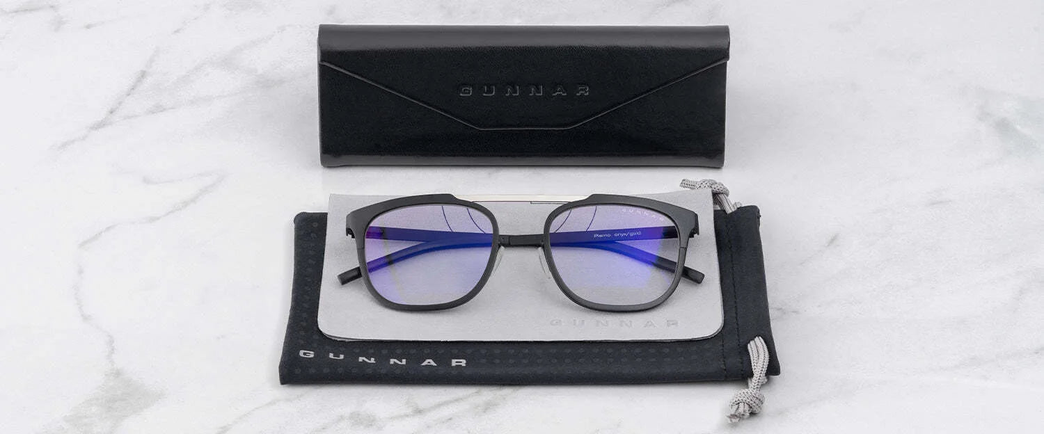 The Gunnar Pismo Computer Glasses | Size 50, by Gunnar, with blue light-filtering lenses, rest elegantly in a black case with a pouch on the marble surface.