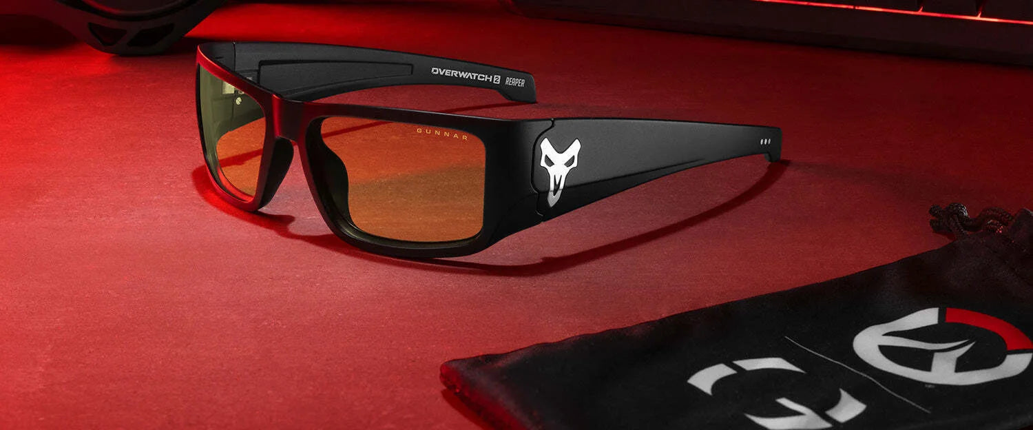 Black Gunnar Overwatch Reaper Computer Glasses with orange-tinted, anti-reflective lenses rest on a red surface, displaying Overwatch logos—perfect for gamers exploring Overwatch 2.