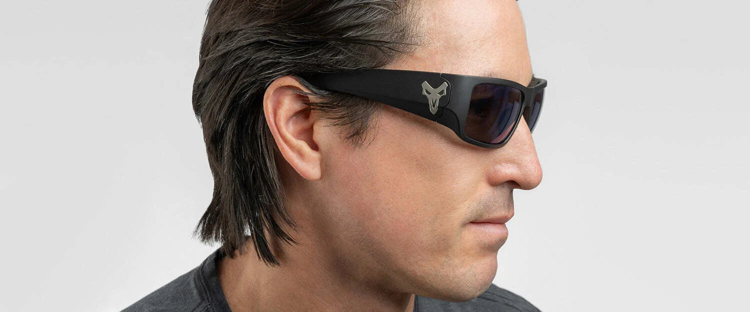 A man wearing Gunnar Overwatch Reaper sunglasses with a logo, looking to the side on a plain background, stylishly blends form and function with blue light-blocking technology.