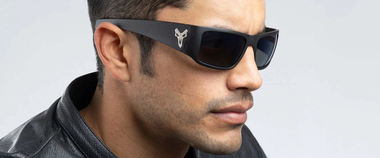 A man, donning dark sunglasses—likely Gunnar Overwatch Reaper Sunglasses (Size 58) known for blue light blocking—and a black leather jacket, is looking to the side against a neutral background.