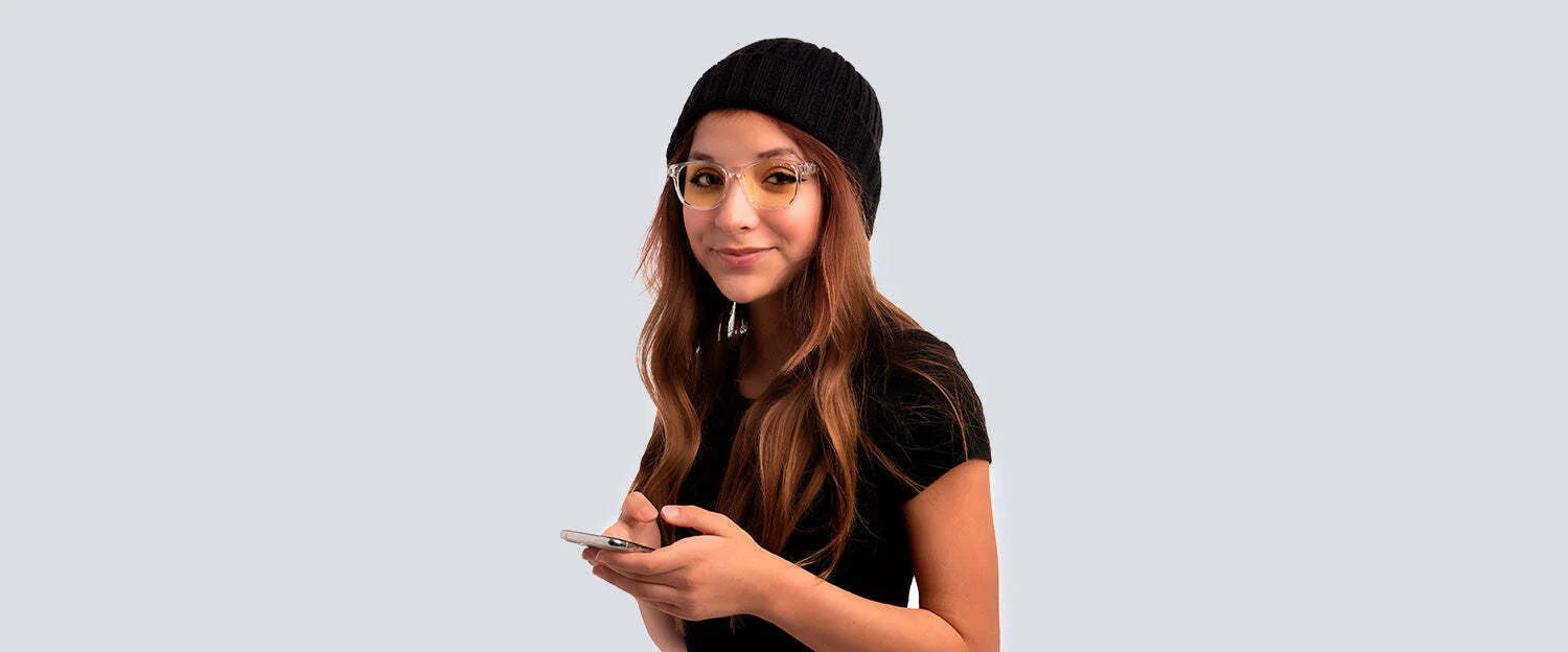 A person with long hair, sporting Gunnar Rush Computer Glasses sized 53 and a beanie, holds a smartphone against a plain background.