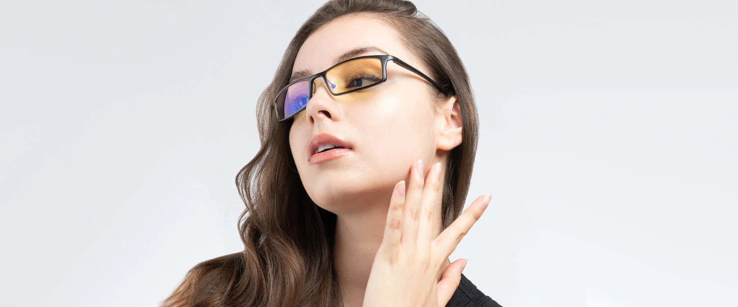 A woman gazes upward against a light background, touching her neck while wearing Gunnar Phenom Computer Glasses in Size 55, featuring advanced optical technology with yellow-tinted lenses to block blue light.