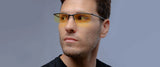 A man wearing Gunnar Emissary Computer Glasses, Size 55, and a black shirt looks to his right against a gray background.